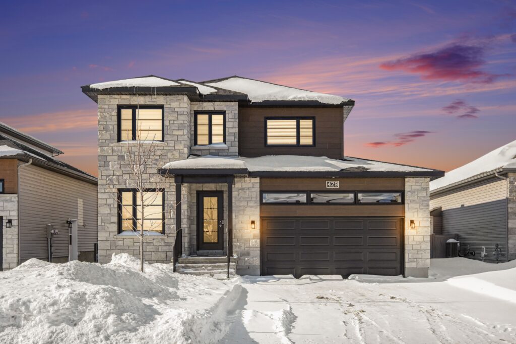 Modern two-storey home on Aurora Street with double garage and snow-covered front yard at sunset by Anna Alemi Real Estate.