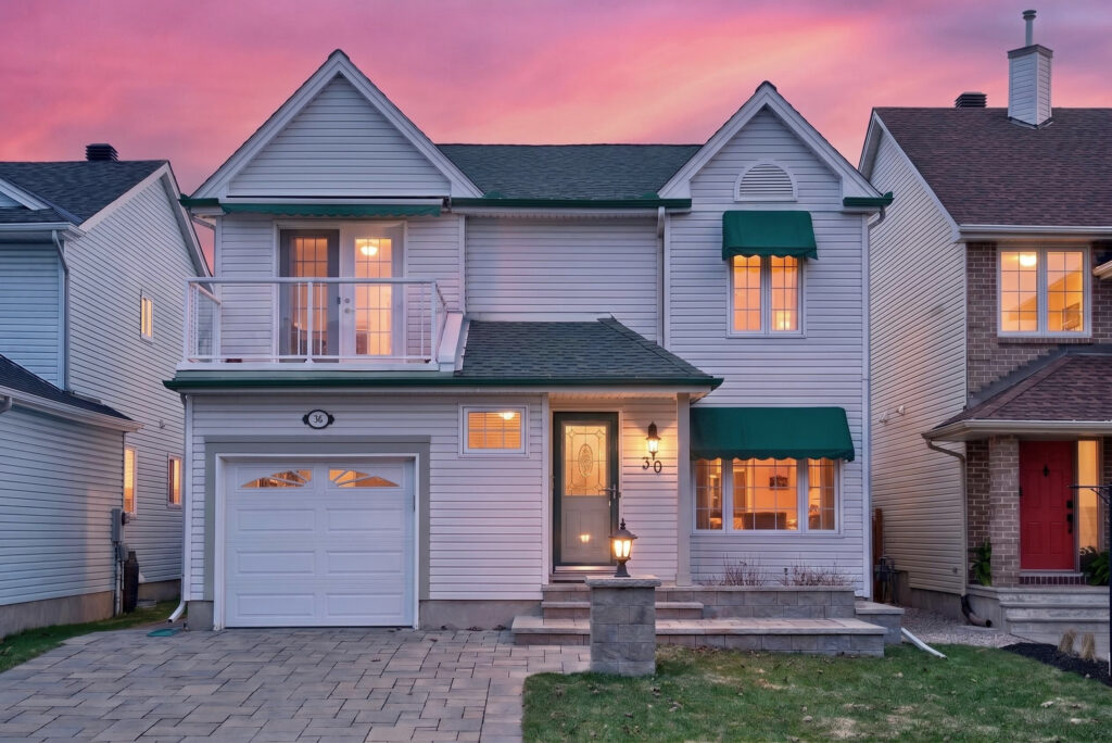 Front exterior of 30 Peacock, a 4-bedroom detached home with stone entry, garage, and landscaped driveway at sunset