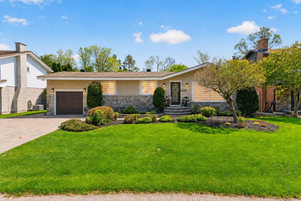 Front exterior of a beautifully updated bungalow with landscaped yard, interlock driveway, attached garage, and mature greenery on a quiet residential street.